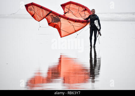 Kitesurfer macht sich auf den Weg vom Ufer aus seinen Kite Durchführung in den Wind zwischen den Surfsessions in Ruhe Bay, Porthcawl, in windigen Bedingungen auf der South Wales Küste. Stockfoto