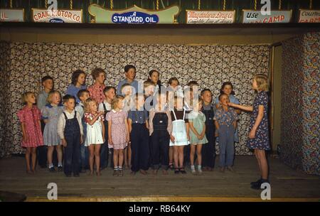 Farbfoto von Schulkindern in Pie Town, New Mexico singen. Über der Bühne Werbung für Craig Motor Co., Standard Oil, und Magahalena Droge Co. sichtbar sind. Vom 1940 Stockfoto