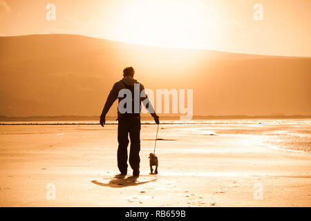 Tywyn Strand, mit Hund Walker, am späten Nachmittag Sonnenschein Stockfoto