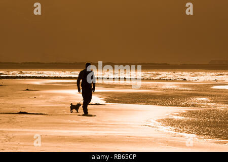 Tywyn Strand, mit Hund Walker, am späten Nachmittag Sonnenschein Stockfoto