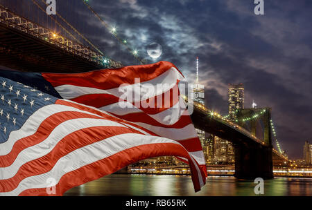 New York City, USA Flagge auf der Brooklyn Bridge bei Sonnenuntergang am Wasser mit Manhattan Skyline im Hintergrund Stockfoto