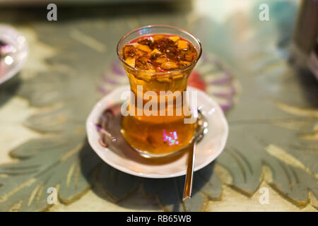 Ein klares Glas Tasse traditionellen Türkischen apfeltee mit Bits von Apple in den Drink auf einem weißen Untertasse mit Teelöffel, Istanbul, Türkei Stockfoto