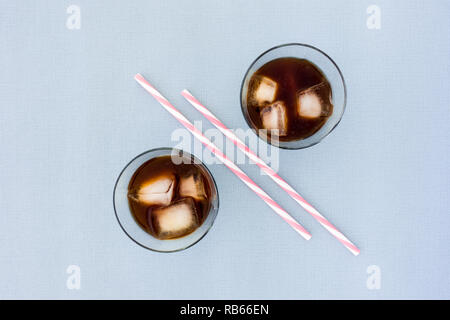 Zwei Strohhalme und zwei Gläser mit Eis Kaffee und Eiswürfel auf blauem Hintergrund mit viel kopieren Raum gefüllt. Ansicht von oben. Stockfoto