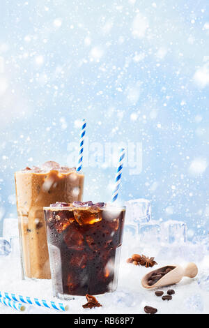 Winter trinke Eiskaffee in einem Glas Kaffee mit Sahne und Eis in ein hohes Glas mit Eiswürfel, Kaffeebohnen und verschiedenen Gewürzen auf Schnee über bl umgeben Stockfoto