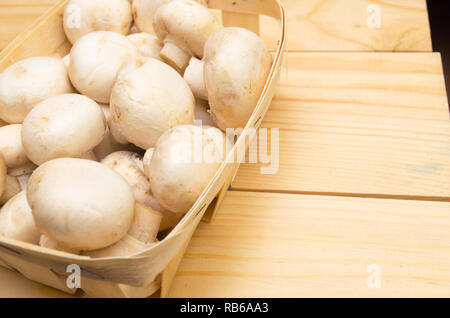 Frische Pilze Champignons in einem Korb auf einem hölzernen Hintergrund Stockfoto