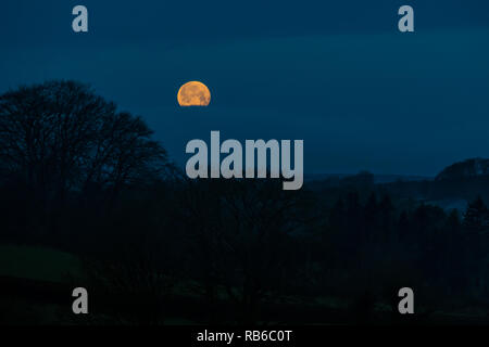 Eine natürliche Szene von einem Vollmond durch einen Bruch in Wolken über einem dunklen ländlichen Landschaft mit Bäumen Stockfoto