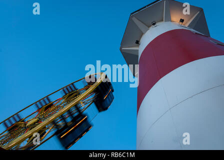 Ein Fahrgeschäft, Spinning, neben einem roten und weißen Turm vor einem blauen Abendhimmel Stockfoto