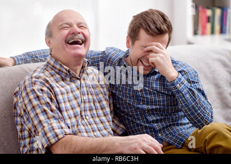 Zwei Männer, die Vater und Sohn sitzen auf dem Sofa im Wohnzimmer zu Hause und die lustige Ereignisse aus der Vergangenheit erinnern. Lachen Sie über den Witz. Gute fa Stockfoto