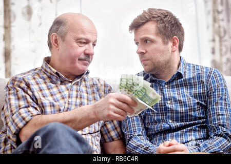 Ältere Vater verleiht Geld zu seinen erwachsenen Sohn. Er hilft seinem Kind befassen sich mit finanziellen Problemen. Stockfoto