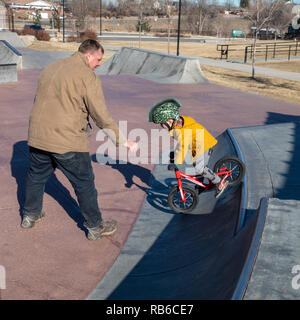 Denver, Colorado - Adam Hjermstad Sr hilft seinem vier Jahre alten Sohn, Adam jr., seine Balance Rad in einem Skatepark zu fahren. Stockfoto