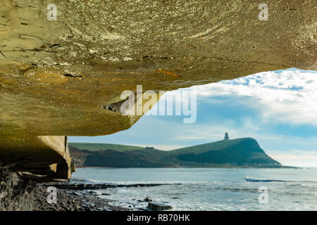 Landschaft Foto von unten Klippe Überhang konzentrierte sich auf Ammonit Körper fossilen mit Clavell Turm im Hintergrund Silhouette an Kimmeri genommen Stockfoto