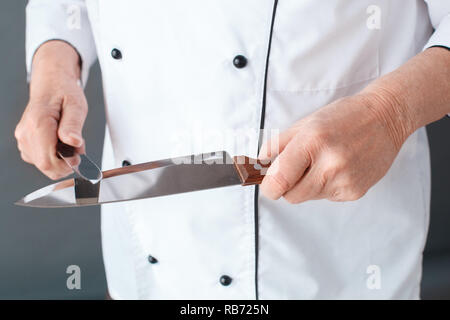 Ältere männliche Koch Studio stehen isoliert auf graue Wand Messerschleifen close-up Stockfoto