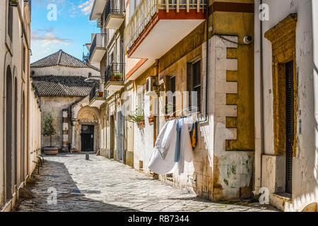 Einer ruhigen Gasse mit Wäsche hängen von einem Fenster führt zum Eingang der Kirche von San Giovanni al Sepolcro in der Stadt Brindisi, Italien Stockfoto