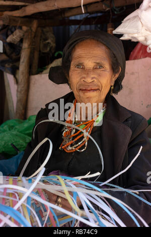 Eine ältere Frau spinnt einen Korb von zerrissen Streifen aus Kunststoff/Hessische gemacht. Sie hat schlechte Zähne durch Kauen Betelnuss und so lächelt nicht. Stockfoto