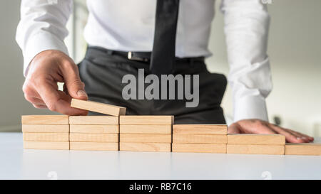 Vorderansicht eines Geschäftsmannes arrangieren Holzwirbel in zu einer Treppe Form in einem konzeptionellen Bild des Unternehmens Vision und Entschlossenheit. Stockfoto