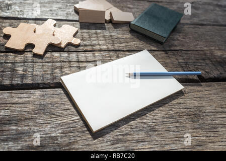 Leere notepad liegen auf einem rustikalen Holztisch mit Bleistift und Puzzles aus Holz und Blöcke auf den Tisch gelegt. Stockfoto