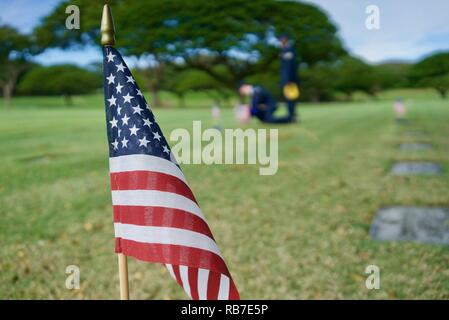 In der Ferne, US Air Force Staff Sgt. Johnnie Anderson und Flieger 1. Klasse Andrew Titus, Zahntechniker mit dem 15 Aeromedical Squadron, statt eine US-Flagge an einem gravemarker in der Nationalen Gedenkstätte Friedhof der Pazifik, Honolulu, Hawaii, Dez. 3, 2016. Anderson und Titus platziert mehrere Markierungen während einer Gedenkveranstaltung zu Ehren der Mut, Service und Opfer des US-Militärs, die während der Angriffe auf Pearl Harbor und Oahu am 7. Dezember 1941 starb. Dez. 7, 2016 ist der 75. Jahrestag der Angriffe und die US-Militärs und Hawaii Stockfoto