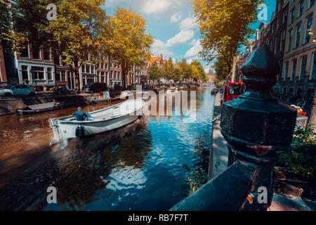 Kanal in Amsterdam im Herbst Sonnenlicht. Boot schwimmend von Bäumen gesäumten Kanal, lebendige Reflexionen, weiße Wolken am Himmel. Niederlande Häuser Wahrzeichen Landschaft Stockfoto