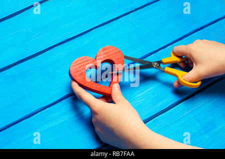 Mädchen schneidet das Herz mit der Schere auf, das Konzept der Abbruch der Beziehungen, Streit und Scheidung. Verrat an den Anderen. blauer Hintergrund Stockfoto