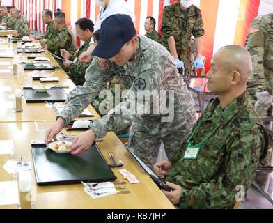 Spc. Nicholas Jerman, 364 Expeditionary Sustainment Command, stellt Japan am Boden zu Verteidigung-kraft Westliche Armee Command Sergeant Major, Command Sgt. Maj. Ryuichi Ichise, mit einem amerikanischen Gericht als Teil der Yama Sakura 71 Iron Chef Schlacht Wettbewerb auf Lager Kengun, Japan, Dez. 5, 2016. Stockfoto