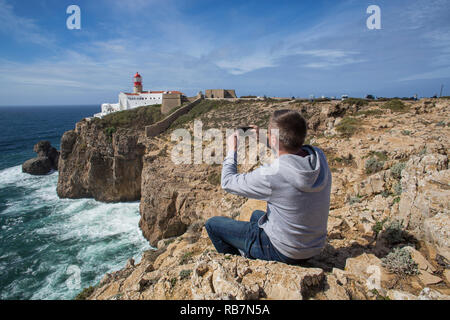 Mann sitzt auf den Fels und unter Foto von Sagres Leuchtturm am Kap St. Vincent. Stockfoto