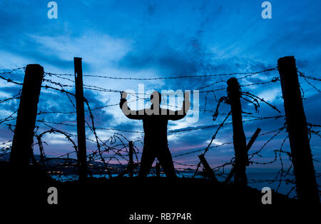 Silhouette des Menschen durch Stacheldraht / Stacheldraht zaun in der Nacht suchen. Brexit, Einwanderung, Asylrecht ... Konzept Stockfoto