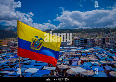 OTAVALO, Ecuador, November 06, 2018: Schöne ecuadorianischen Flaggen schwenkten in einem wunderschönen sonnigen Tag mit Hütten in der Straße Markt in Otavalo entfernt mit einem Berg hinter in Otavalo. Stockfoto