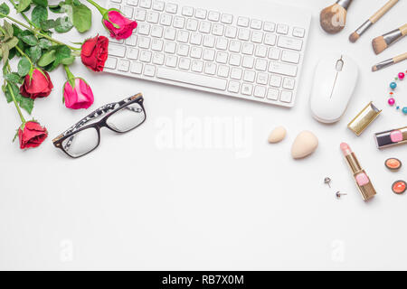 Schreibtisch mit kabelloser Tastatur und Mous, rosa und rote Rosen Blumenstrauß, Frauen Kosmetik auf weißem Hintergrund. Flach. Ansicht von oben. Valentine's workin Stockfoto