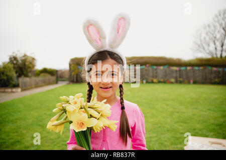 Porträt eines jungen Mädchens stehen im Freien, während Sie ein Bündel Narzissen und tragen Rabbit Ears. Stockfoto