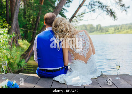 Rückseite des Bräutigam und Braut sitzen nebeneinander auf der Brücke in der Nähe des Sees. Stockfoto