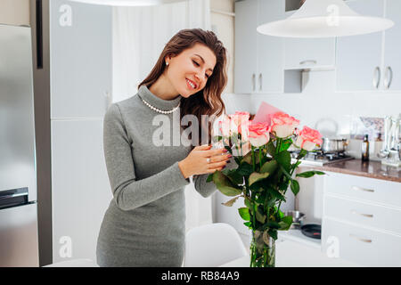 Junge Frau gefunden Blumenstrauß aus Rosen geschmückt mit Karte auf Küche. Happy girl lesen Hinweis in den Blumen. Valentines Tag Stockfoto