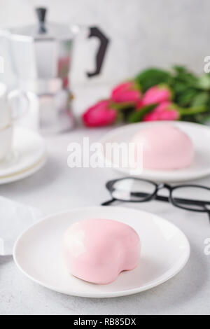 Trendy mousse Kuchen mit rosa Spiegel Glasur. Herzförmige behandelt für Valentinstag. Blumen im Hintergrund. Stockfoto