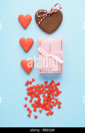 Valentinstag kreative Layout Design. Geschenkbox mit Schleife, rote herzförmige Plätzchen, Baisers und Süßigkeiten. Pastell rosa und blauen Farben. Flach. Stockfoto