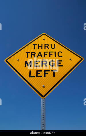 Die "Thru Traffic Merge Left' street sign in der kalifornischen Sonne. Stockfoto