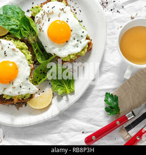 Ansicht von oben Gesunde avocado Toast zum Frühstück oder Mittagessen mit Roggenbrot, Avocado pürieren, Toast und Spiegelei auf weißem Hintergrund mit Tasse Tee. Delicio Stockfoto