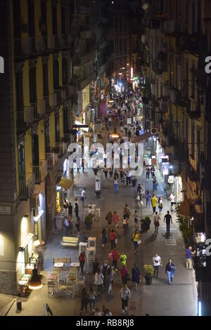 Nacht das Leben auf der Straße in Neapel. Massen von Menschen zu Fuß in gepflasterten Fußgängerzone zwischen typischen hohen Wohnblocks der Mediterranen mit kleinen Sh Stockfoto