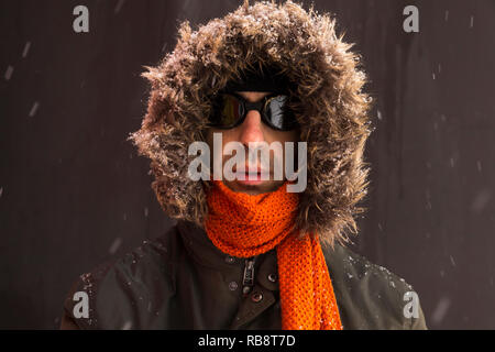 Porträt von einem einzigen männlichen winter Abenteurer das Tragen eines warmen grünen Mantel mit Fell Kapuze, einen blauen ski Mütze, Schal und eine Orange Schwarz retro style Schutzbrille Stockfoto