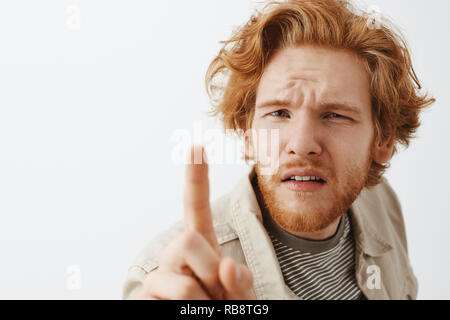 Headshot von verwirrt und fragte fröhlich Rothaarige mit unordentlichen Haar und Bart schielen und biegen in Richtung und stossen Kamera mit Zeigefinger unsicher und misstrauisch runzelte ungewiss Stockfoto