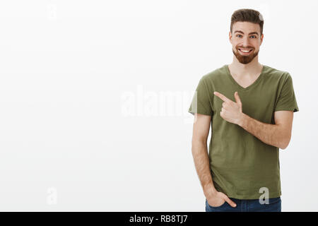 Beeindruckt und sehr glücklich, bärtigen Mann mit tiefen blauen Augen in t-shirt, auf der linken oberen Ecke überrascht oder hinter zufrieden Lächeln aufgeregt über unglaubliches Produkt erzählen auf weißem Hintergrund Stockfoto