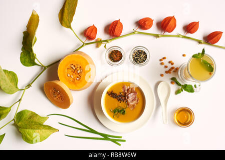 Flach orange Creme Suppe mit Fleisch und Tee mit Minze für die Gäste im luxuriösen Restaurant zubereitet. Kürbis und Physalis liegen in der Nähe von Essen. Oben Blick auf gesundes Essen mit Dekor auf der weißen Tischdecke. Stockfoto