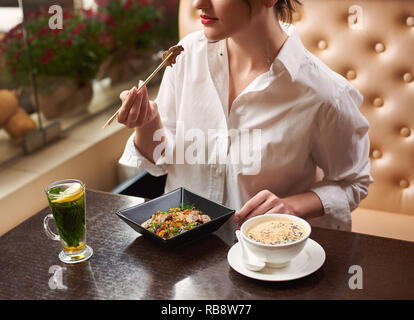 Croped weiblichen Kunden bestellen orientalischen Stil Mahlzeit im Restaurant, Mittagessen inklusive Suppe mit Samen, warmer Salat mit Fleisch und Zitrone Minze Tee. Weibliche gut gepflegte Hände halten Futtersticks. Stockfoto