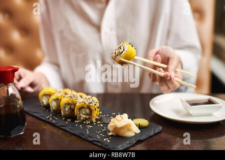 Frau genießen Sie Sushi in Luxus Restaurant. Weibliche client Holding Futtersticks und Essen orientalische Speisen auf das Mittagessen. Getreide der traditionelle japanische Gerichte mit Wasabi und Ingwer mariniert. Stockfoto