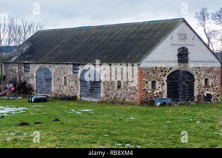 Ein wenig Schnee auf der grünen Weide. Verlassene Scheune auf einem verlassenen Bauernhof. Beginn des Winters in Europa. Stockfoto