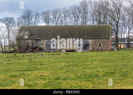 Ein wenig Schnee auf der grünen Weide. Verlassene Scheune auf einem verlassenen Bauernhof. Beginn des Winters in Europa. Stockfoto