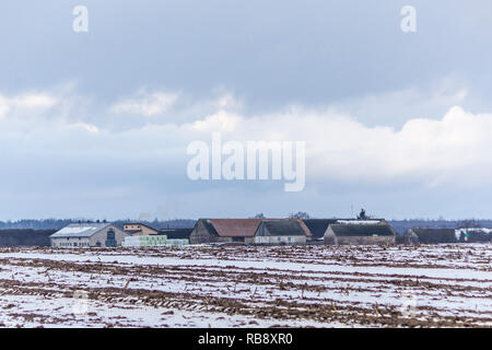 Ein wenig Schnee auf Ackerland. Molkerei Scheunen. Weiß und Blau Rollen von Heu und Silage in der Nähe von Scheunen. Beginn des Winters in Europa. Stockfoto