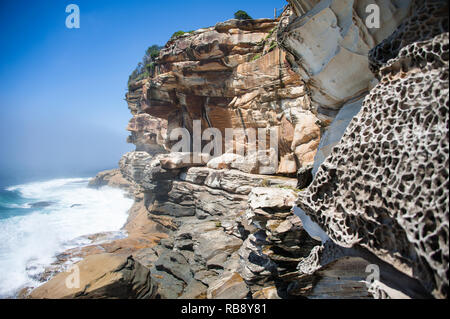 Dramatische Felsformationen von Wind und Wasser in der Nähe von Bondi Beach, Sydney, Australien erodiert. Farbige Sandsteinklippen gegen blaue Meer/Himmel Hintergrund Stockfoto