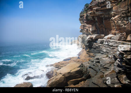 Dramatische Felsformationen von Wind und Wasser in der Nähe von Bondi Beach, Sydney, Australien erodiert. Farbige Sandsteinklippen gegen blaue Meer/Himmel Hintergrund Stockfoto