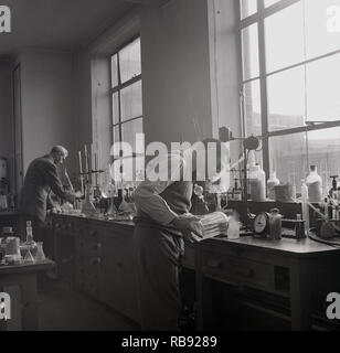 1950, historische, zwei männliche Wissenschaftler arbeiten mit Chemikalien an einer Werkbank in einem chemielabor an der Universität Oxford, England, UK.
