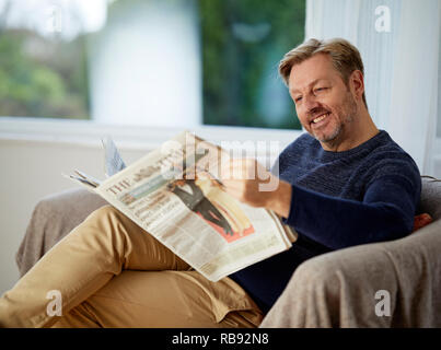 Mann entspannt auf einem Sofa lesen ein Papier Stockfoto