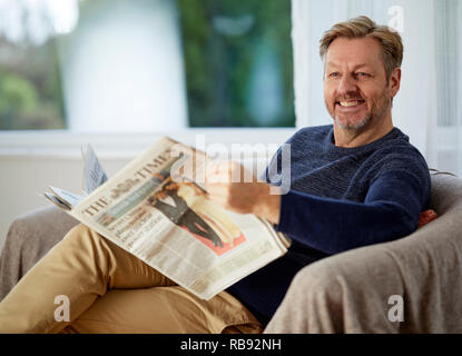 Mann entspannt auf einem Sofa lesen ein Papier Stockfoto